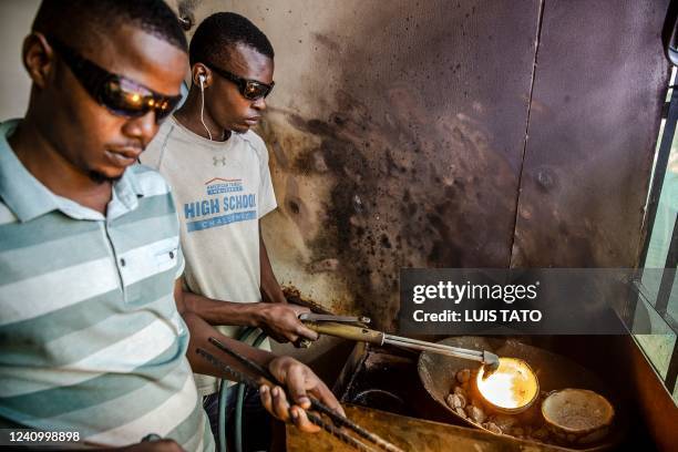 Two men melt pure gold fragments coming from different mines in the region, at a gold market in Geita, Tanzania on May 28, 2022. - Tanzania is a land...