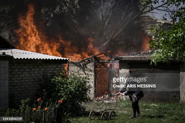 An elderly woman walks away from a burning house garage after shelling in the city of Lysytsansk at the eastern Ukrainian region of Donbas on May 30...