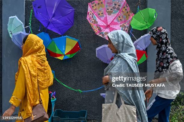Women walk past the umbrellas displayed for sale along a street in Srinagar on June 1, 2022.