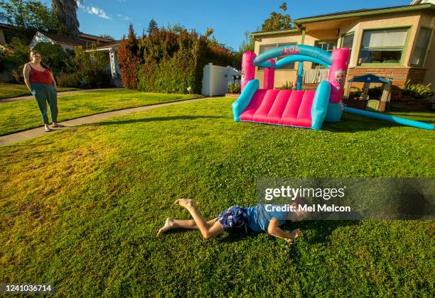 Jay Bass rolls over and over while playing on the front lawn of his home on Moreno Ave. In Brentwood. In background looking on is his mother Sasha...