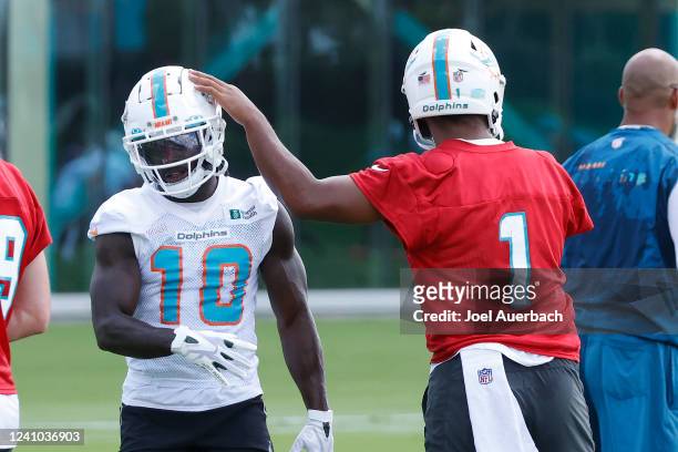 Tua Tagovailoa taps the helmet of Tyreek Hill of the Miami Dolphins between drills during the Miami Dolphins Mandatory Minicamp at the Baptist Health...