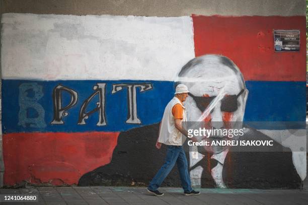 Pedestrian walks past a partly vandalized mural depicting Russian President Vladimir Putin in Belgrade on June 2, 2022. - At a time when most...