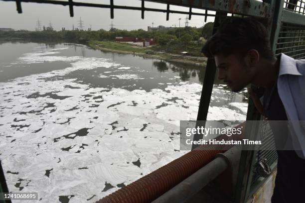 Man looking at the white froth flaoting in polluted Yamuna River at ITO Chhath Ghat on June 2, 2022 in New Delhi, India. While only 2% of Yamuna...