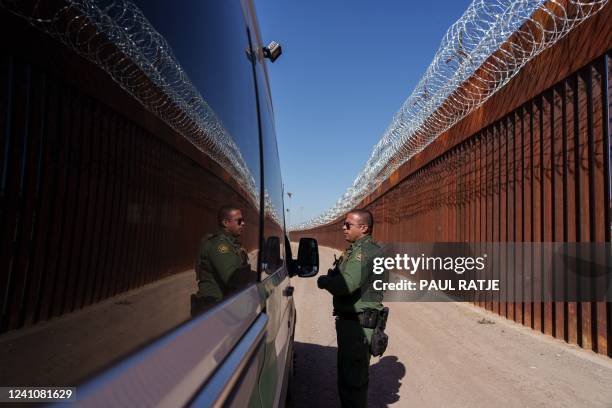 United States Border Patrol agent Carlos Rivera is reflected in the window of a vehicle as he speaks to another agent along the border wall in...