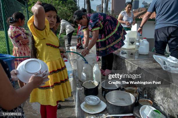 Maria Lubia goes to fill two water cans at the spring that feeds the camp, a water tap with a low flow, on Dec. 15 in Bogota, Colombia. Other women...