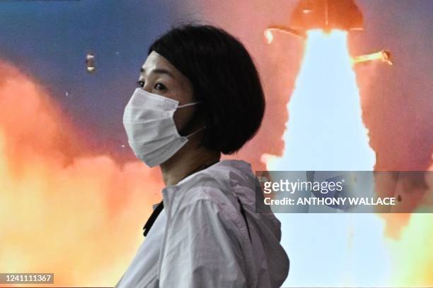 Woman walks past a screen showing a news broadcast with file footage of a North Korean missile test, at a railway station in Seoul on June 5, 2022. -...