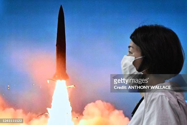 Woman walks past a screen showing a news broadcast with file footage of a North Korean missile test, at a railway station in Seoul on June 5, 2022. -...