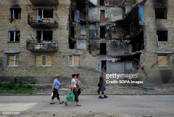 People carry humanitarian aid past a destroyed apartment building that was damaged as a result of the shelling of the Russian army in the village of...