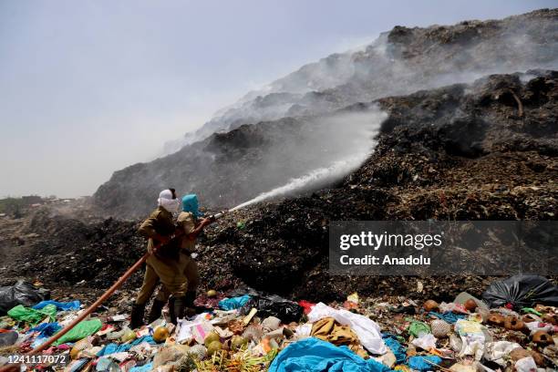 Firefighters try to douse a fire as smoke billows from a garbage mound after a fire at Bhalswa landfill on the outskirts of New Delhi, India on June...