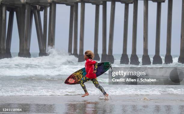 Huntington Beach, CA Matthew Oliveira runs out to compete in the junior surf competition during A Great Day in the Stoke at the Huntington Beach pier...