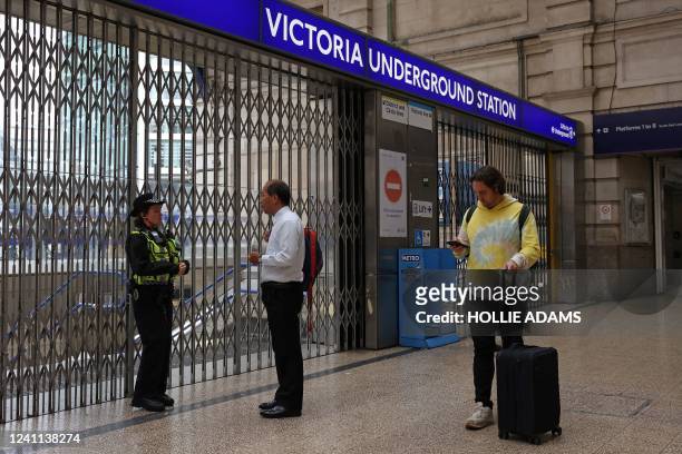 Police officer talks to a commuter at the shuttered entrance to Victoria underground tube station in London on June 6 during a 24-hour strike by...