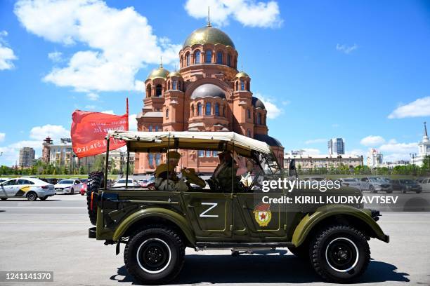 Tourists wearing WWII-era styled outfit take a city tour in a historical military vehicle adorned with the letter Z, which has become a symbol of...
