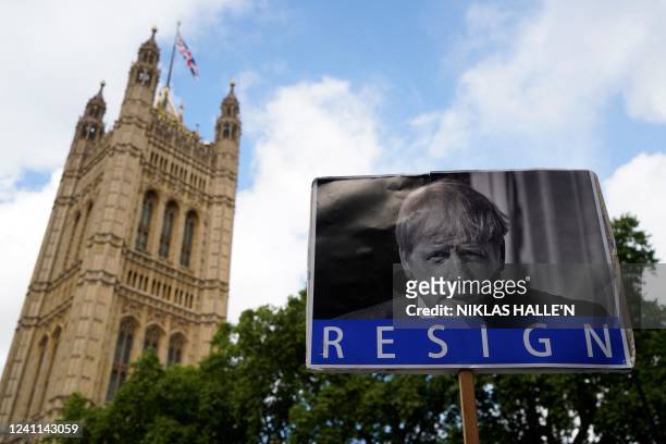 Photograph taken on June 6, 2022 shows a board reading "Resign" and picturing Britain's Prime Minister Boris Johnson in front of The House of...