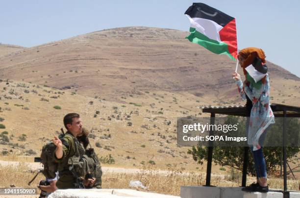 An Israeli soldier prevents a Palestinian protester from raising a Palestinian flag while standing at an observation point at an Israeli checkpoint,...