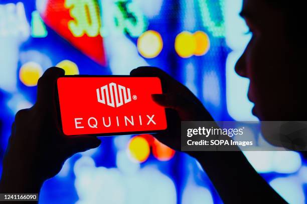 In this photo illustration, a silhouetted woman holds a smartphone with the Equinix, Inc. Logo displayed on the screen.
