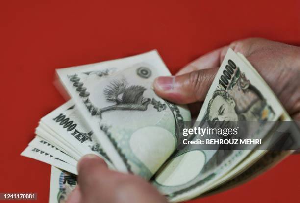 This photo illustration shows a person counting out Japanese 10,000 yen banknotes in Tokyo on June 8, 2022. The dollar fetched 133.03 yen in Asian...