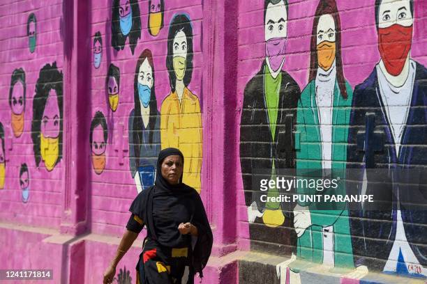 Woman walks past a mural depicting people wearing facemasks to create to awareness about the Covid-19 coronavirus in Mumbai on June 8, 2022.