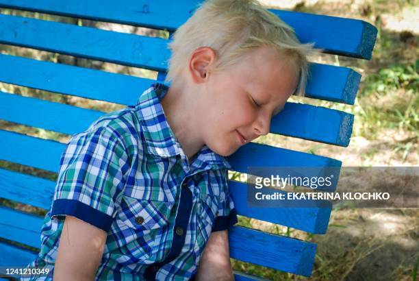 Eight-year-old internally displaced boy, Egor Kravtsov closes his eyes resting on a bench during an interview with AFP in Zaporizhzhia, southern...