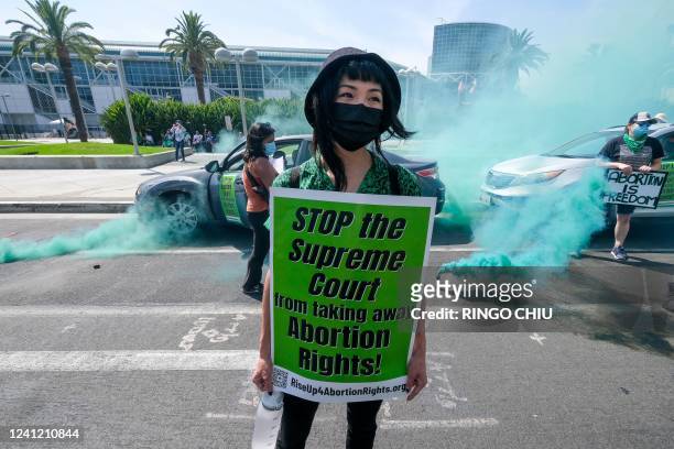 An Abortion Rights protester holds a sign as green colored smoke is released during an Abortion Rights protest outside the 9th Summit of the Americas...