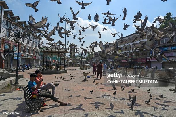 People sit on a bench along a street during a strike in Srinagar on June 10, 2022. - A spontaneous strike was observed in Srinagar to protest against...