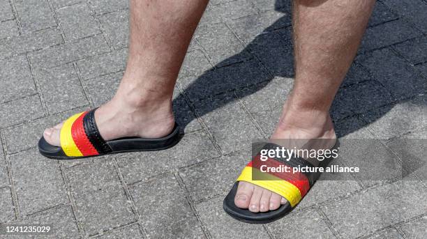 May 2022, Schleswig-Holstein, Pelzerhaken: A man wears bathing slippers in the German national colors black-red-gold. Photo: Markus...
