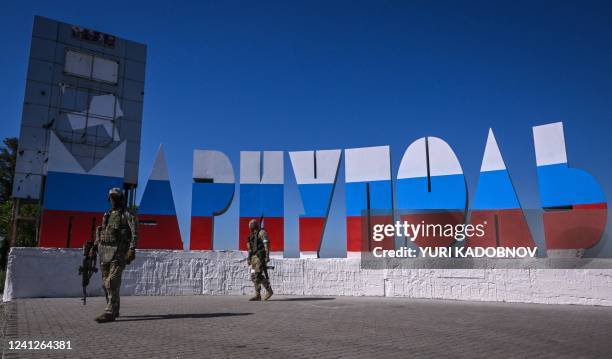 Russian servicemen walk near the welcome sign "Mariupol", which has been painted in Russian flag colours, at the entrance of Mariupol on June 12 amid...