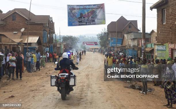 Illustration shows a welcome banner and lots of people along the road on the way to a visit to the Panzi hospital, part of an official visit of the...