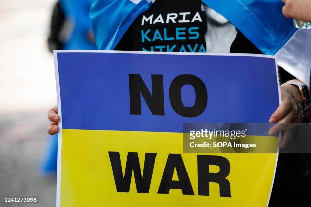 Protester wearing a t-shirt with the name of Belarusian opposition leader and political prisoner Marya Kalesnikava holds a placard reading "No war"...