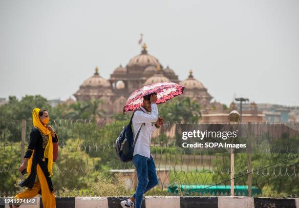 Man shelters under an umbrella as he walks past the Akshardham temple as New Delhi experiences a heat wave. Temperatures in the Indian capital soared...