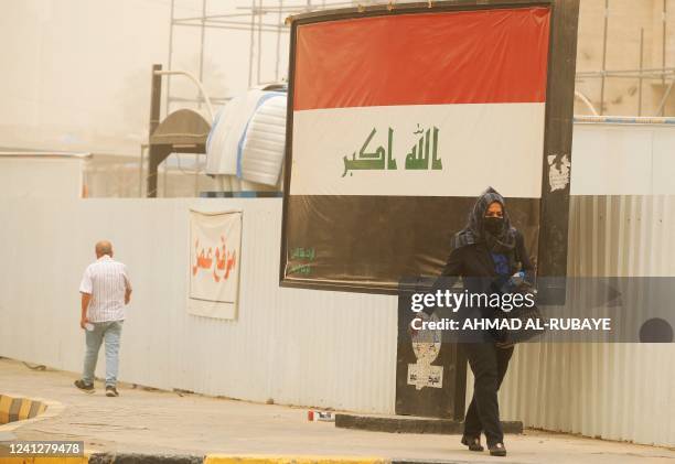 Woman covers her face as she walks past a national flag in Baghdad with white dust covering the Iraqi capital and surrounding areas on June 13, 2022...