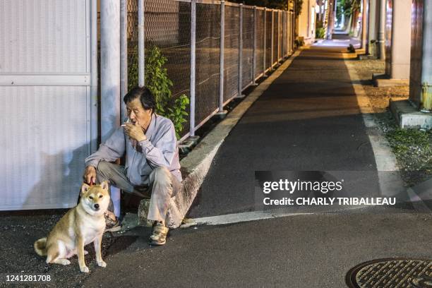 Man, flanked by his shiba inu dog, smokes a cigarette along a street at night in Suita, Osaka prefecture on June 13, 2022.