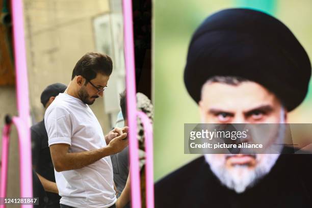 June 2022, Iraq, Sadr City: A man stands on the street near a poster bearing the picture of Iraqi Shia cleric Muqtada al-Sadr. Iraqi lawmakers of the...