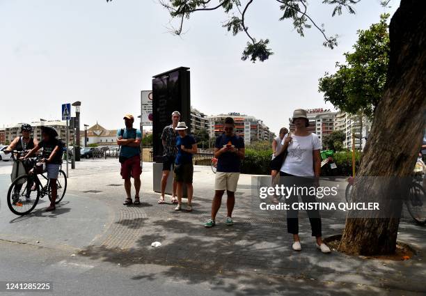 People wai in the shade to cross a street during a heatwave in Seville on June 13, 2022. - Spain was today already in the grips of a heatwave...