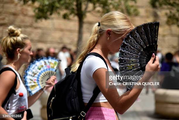 Two women use fans to fight the scorching heat during a heatwave in Seville on June 13, 2022. - Spain was today already in the grips of a heatwave...