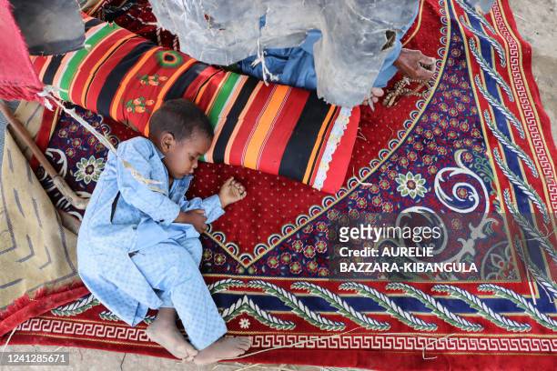 Boy takes a nap while lying on a carpet and sheltering from the sun under veils at the nomadic camp in Toukra in N'Djamena, Chad, June 10, 2022. - In...