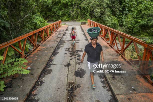 Woman carrying household items and her daughter cross a bridge to get home in San Vicente. According to the Food and Agriculture Organization of the...