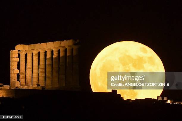 This photograph shows a full moon, known as the "Strawberry Moon", behind the Temple of Poseidon at Cape Sounion, south of Athens, on June 14, 2022.