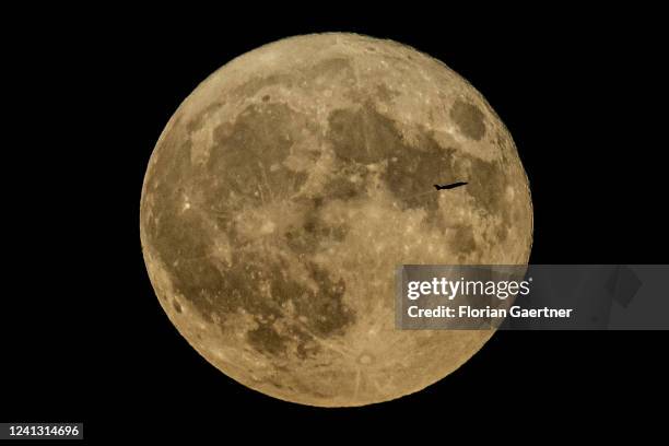 The silhouette of a plane is pictured in front of the so called strawberry moon on June 14, 2022 in Berlin, Germany.