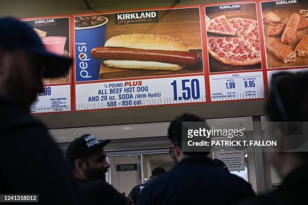 Customers wait in line to order below signage for the Costco Kirkland Signature $1.50 hot dog and soda combo, which has maintained the same price...