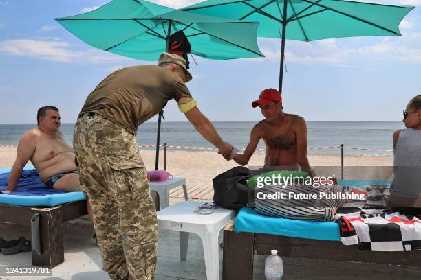 Serviceman gives a man a summons to appear at a military registration and enlistment office to a man during a raid on a beach in Odesa, southern...