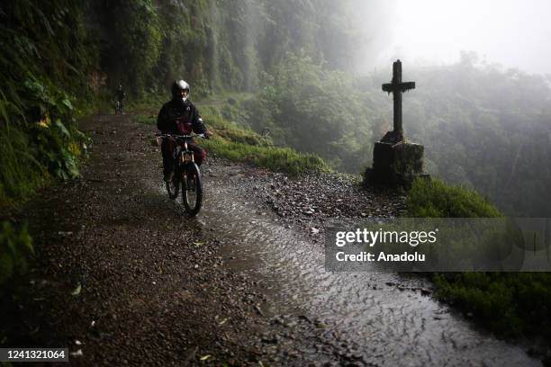 Tourist rides a bicycle next to a cross that represents that someone died in that place on the Death Road in Los Yungas, La Paz, Bolivia on June 07,...