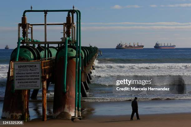 Man walks on the beach next to oil pipelines of the Ventanas industrial park on June 14, 2022 in Puchuncavi, Chile. Due to the high pollution,...