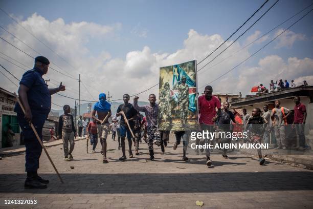 Policeman gives thumbs up as demonstrators carry a poster honouring the Democratic Republic of Congo armed forces during a protest in Goma on June...