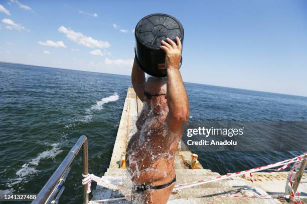 People collect water from the sea using buckets with ropes and douse themselves, as swimming in the sea is prohibited due to the threat of mines, in...