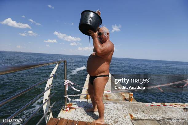 People collect water from the sea using buckets with ropes and douse themselves, as swimming in the sea is prohibited due to the threat of mines, in...