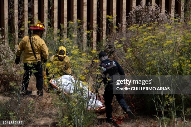 Firefighters carry the body of an alleged smuggler murdered near the US-Mexico border wall in Tijuana, Baja California state, Mexico, on June 15,...