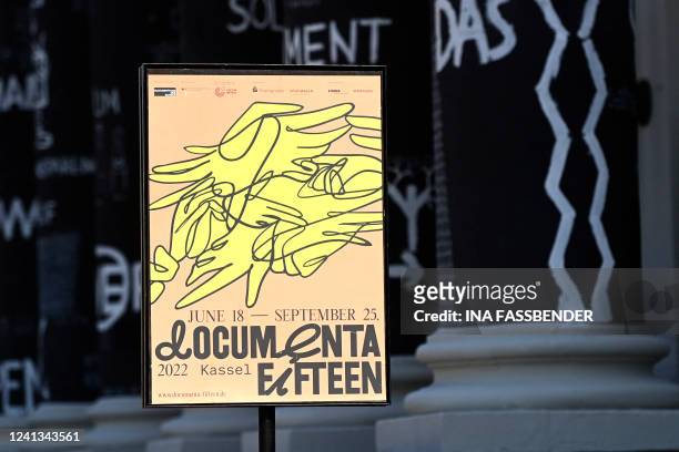 Photo shows a placard of the documenta fifteen contemporary art exhibition in front of black painted columns with drawings by Romanian artist Dan...