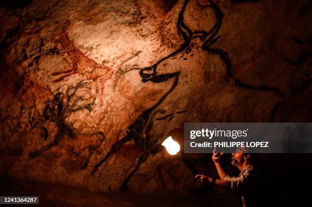 An employee shows paintings inside the life size Lascaux cave replica during a special immersive torch light visit on June 16, 2022 in Montignac.
