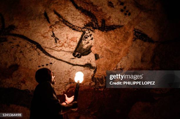 An employee shows paintings inside the life size Lascaux cave replica during a special immersive torch light visit on June 16, 2022 in Montignac.