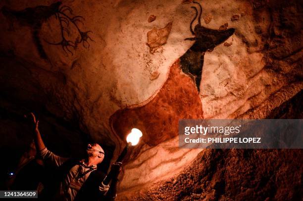 An employee shows paintings inside the life size Lascaux cave replica during a special immersive torch light visit on June 16, 2022 in Montignac.